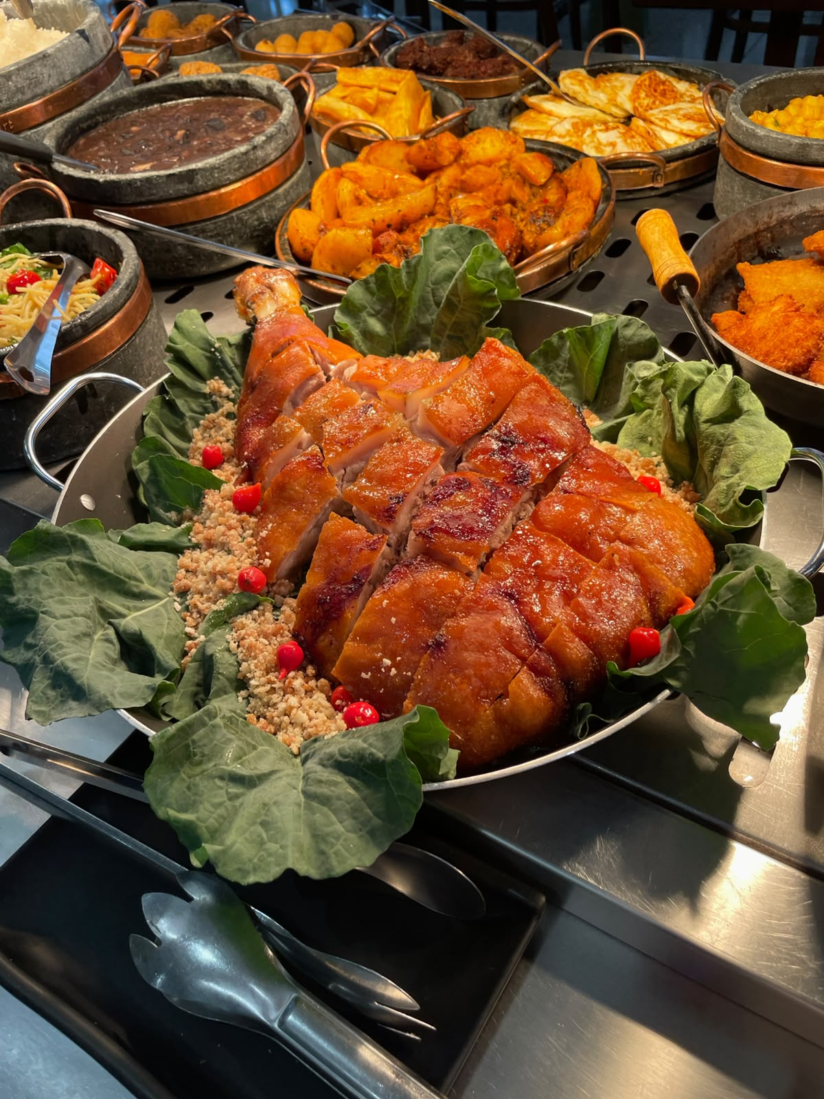 Pernil assado inteiro com farofa e couve, cercado de guarnições no buffet