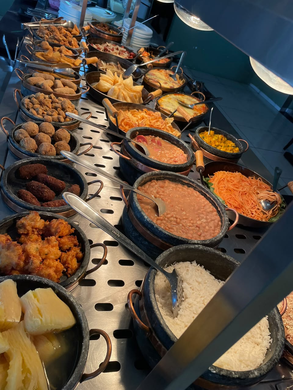 Balcão do buffet com salgados, bolinhos, feijoada, feijão e massas em panelas de pedra